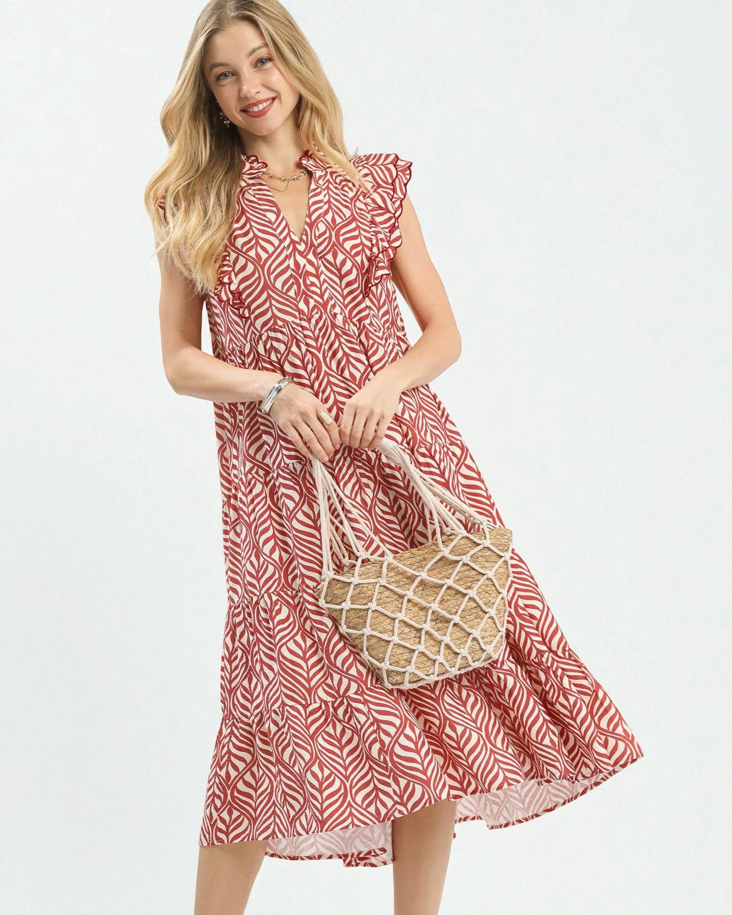 Woman wearing a red and white patterned dress holding a straw bag on a white background