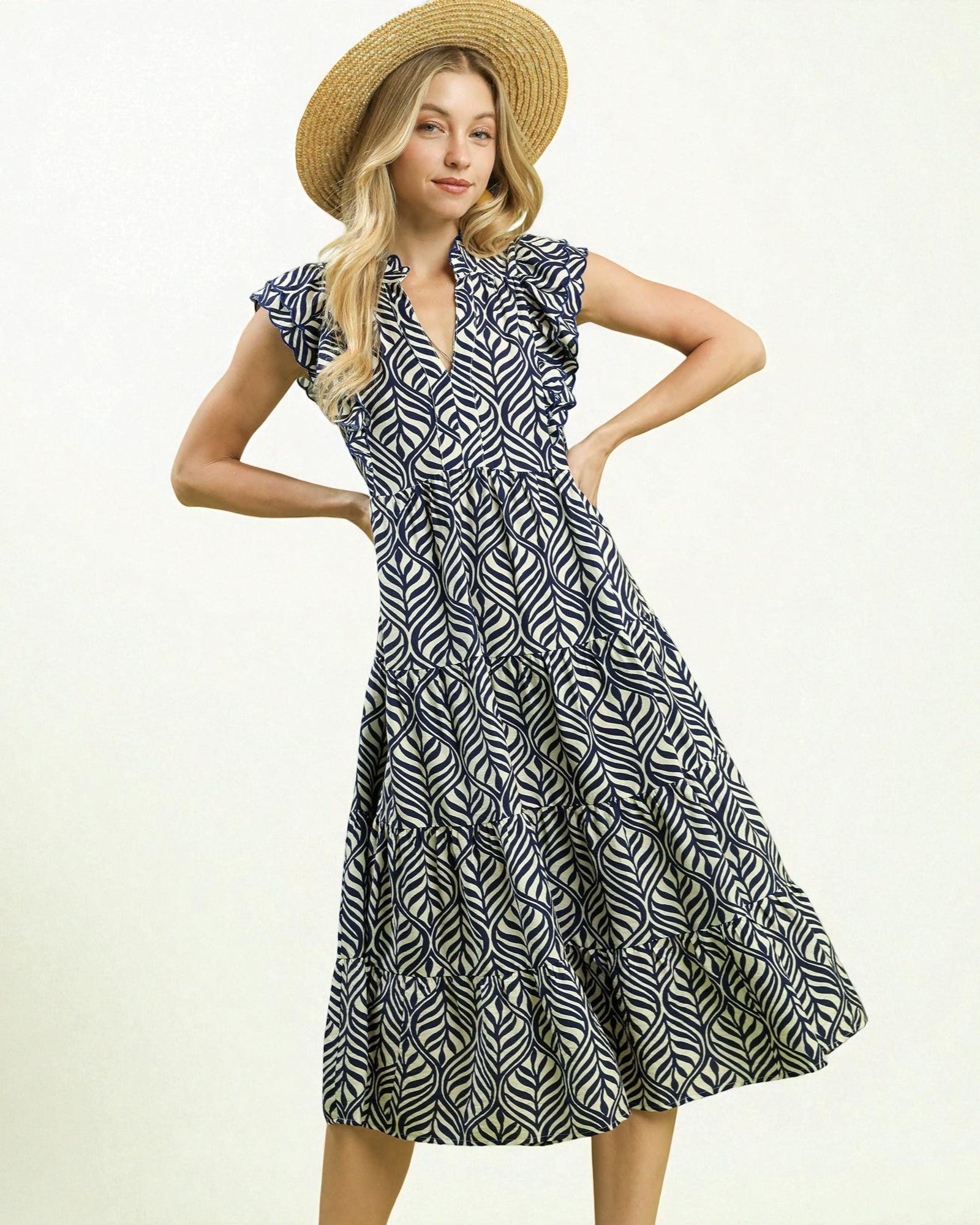 Woman wearing a black and white patterned dress with a straw hat on a light background