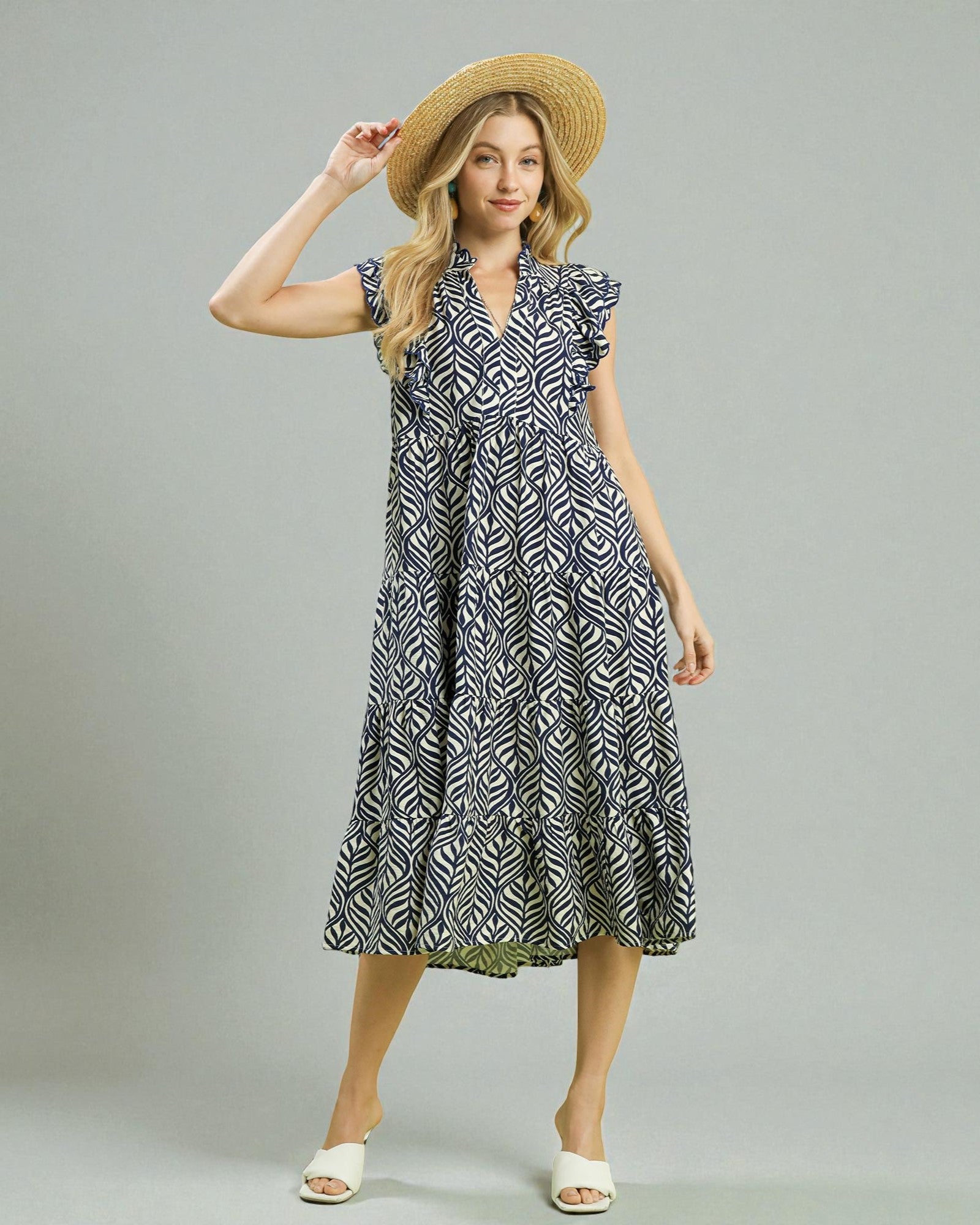 Woman wearing a patterned dress and straw hat on a plain background