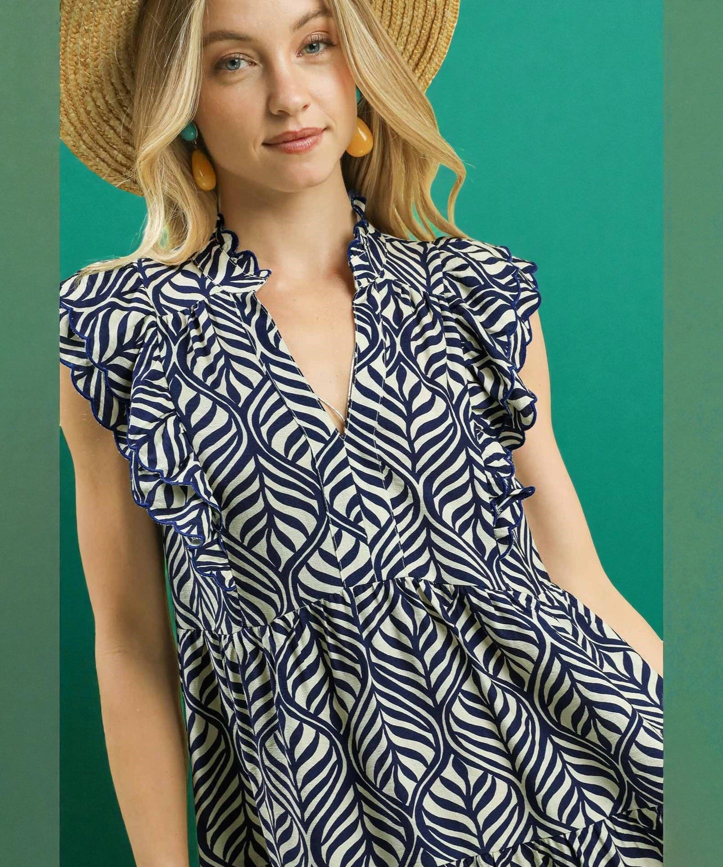 Woman wearing a navy and white patterned dress with a straw hat against a teal background