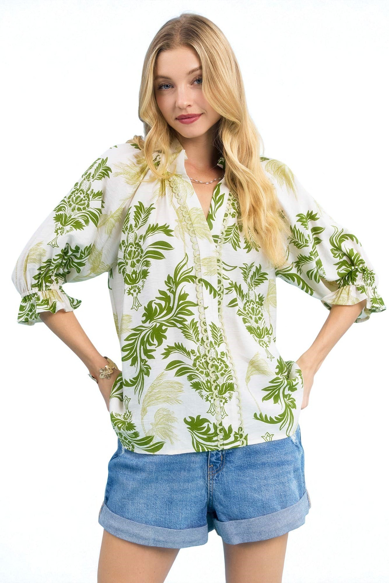 Woman wearing a white blouse with green floral pattern and denim shorts on a white background