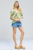 Woman wearing a green floral blouse and denim shorts on a white background