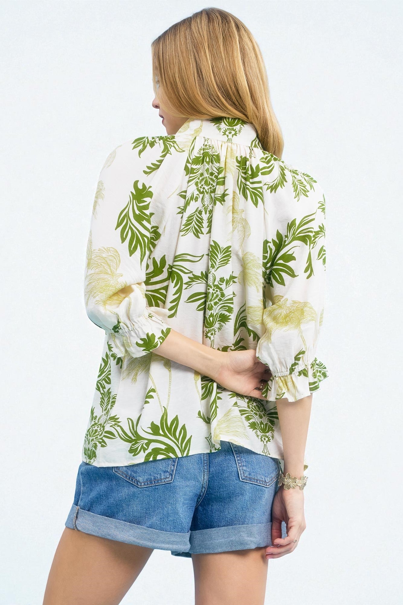 Woman wearing a white blouse with green floral patterns and denim shorts on a white background