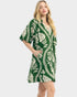 A woman modeling a short-sleeve, V-neck dress with a green and cream botanical leaf pattern, set against a solid light gray background.