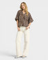Woman wearing a leopard print blouse and white pants on a white background