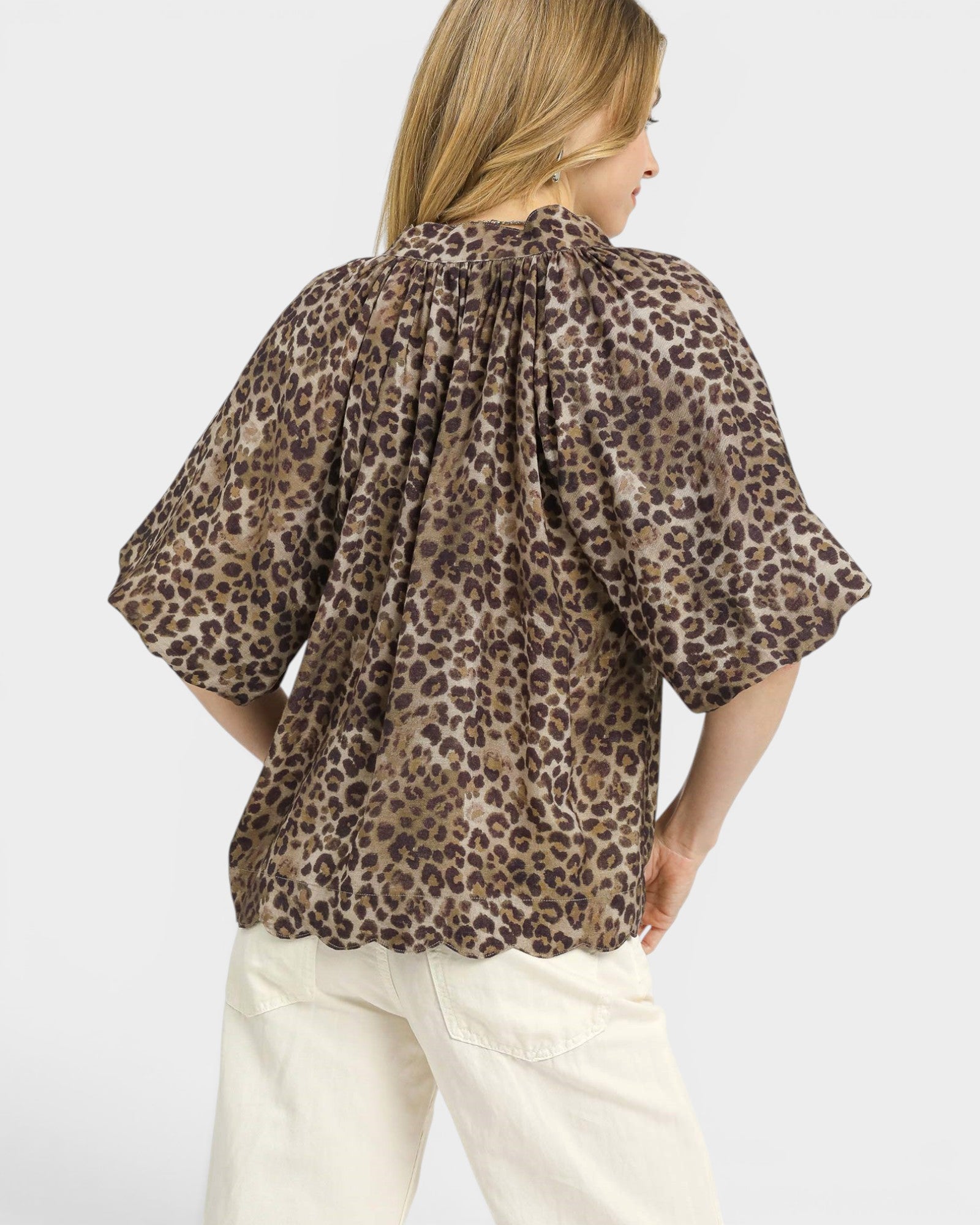 Woman wearing a leopard print blouse and white pants on a light gray background