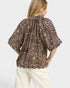 Woman wearing a leopard print blouse and white pants on a light gray background