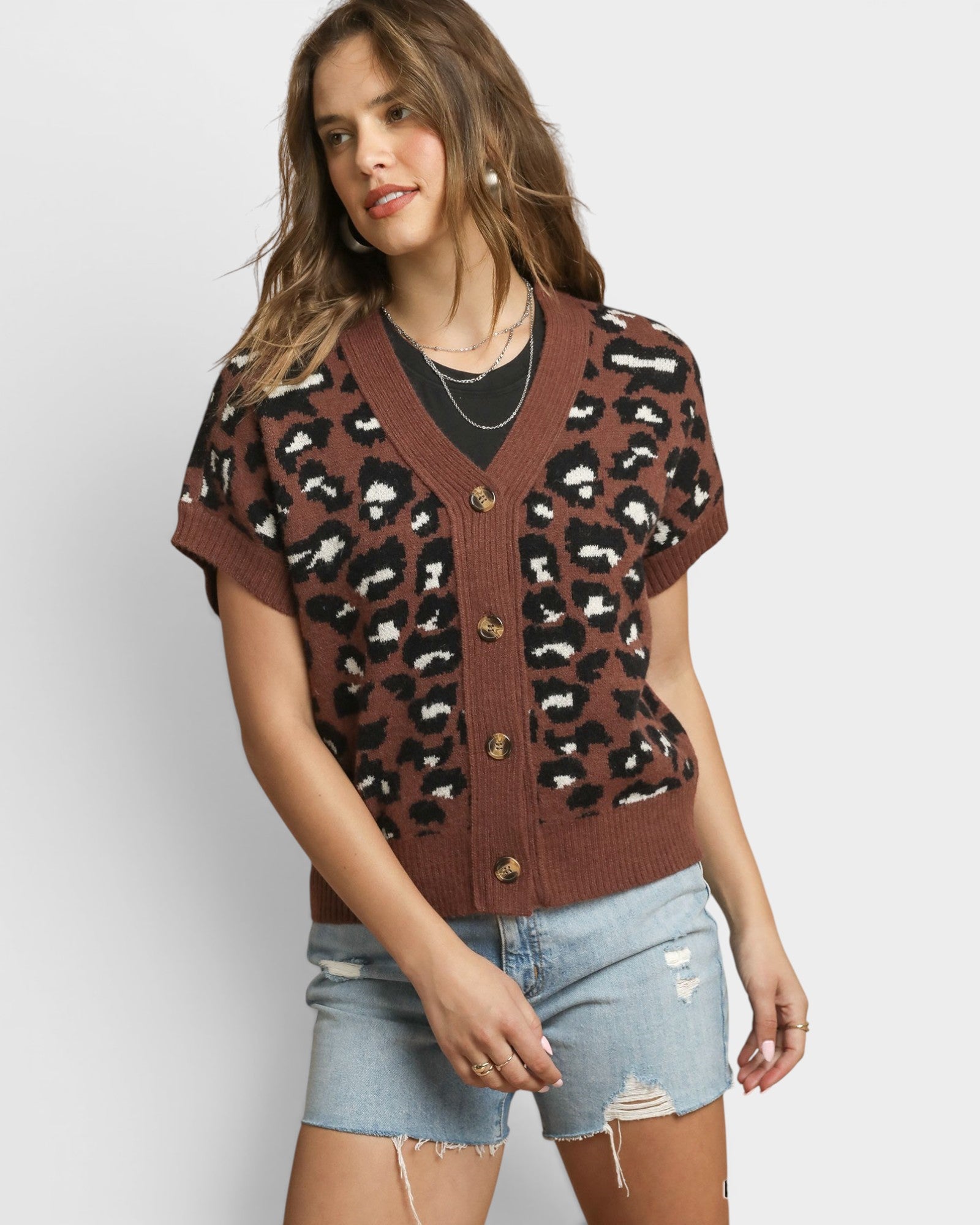 Woman wearing a leopard print cardigan and denim shorts on a white background