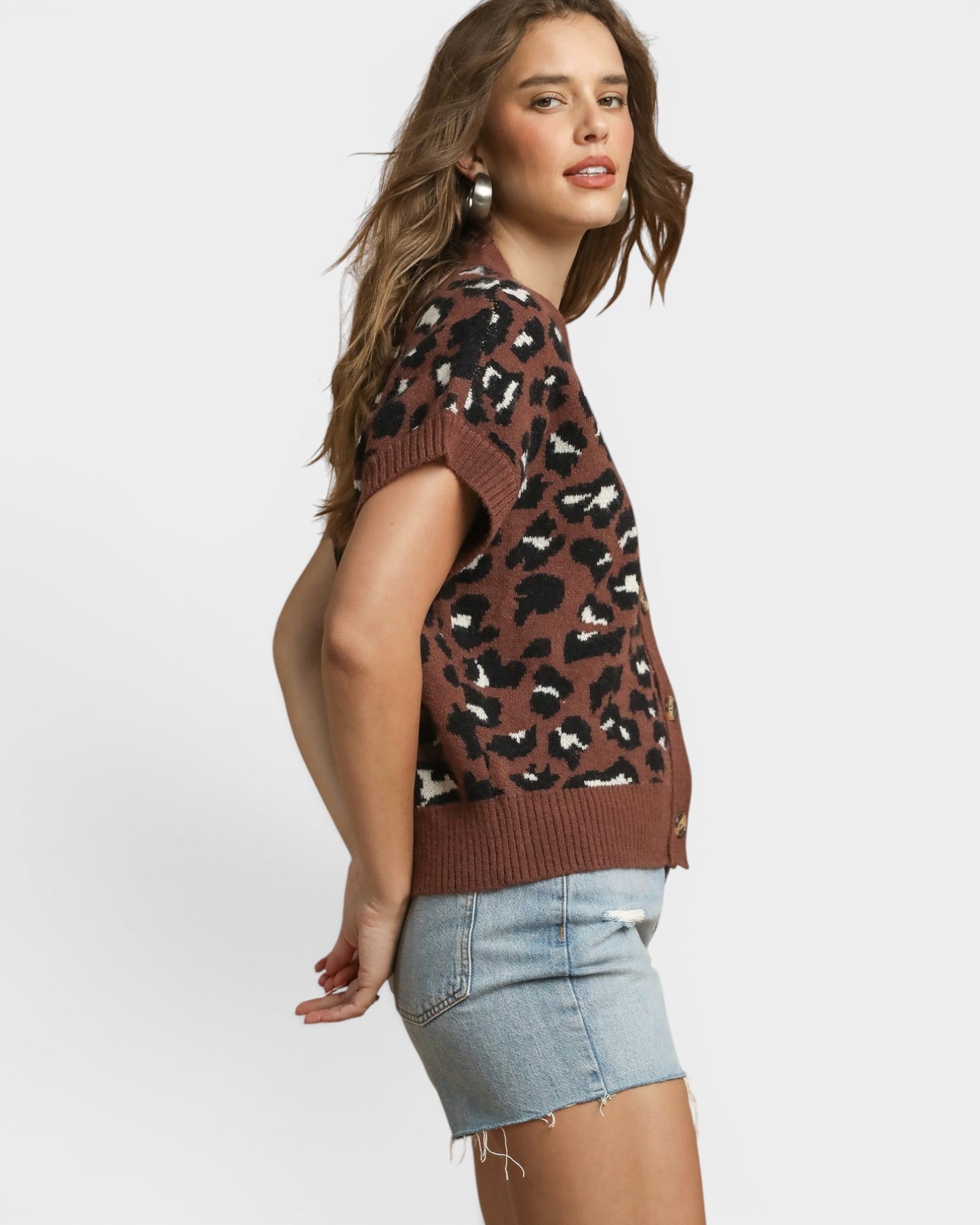 Woman wearing a brown leopard print sweater vest and denim shorts on a white background