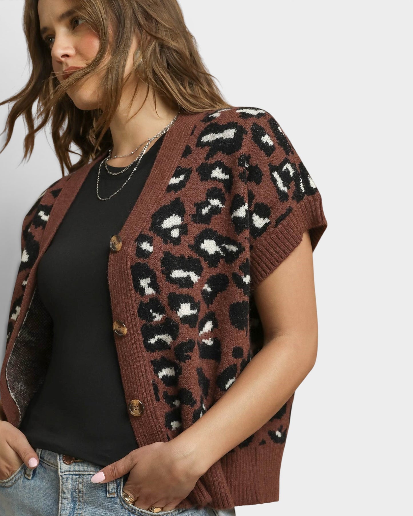 Woman wearing a leopard print cardigan over a black top and jeans on a plain background