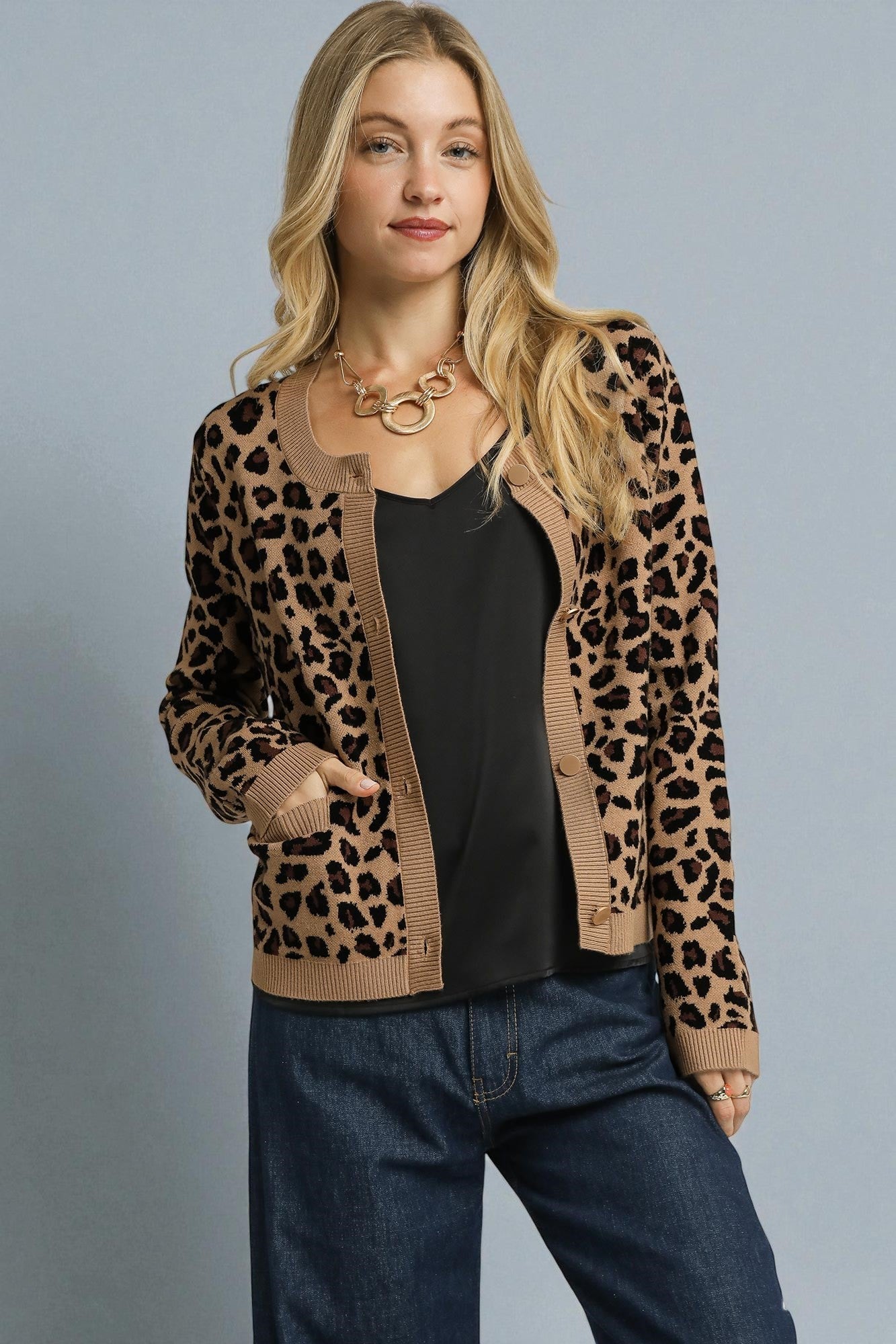 Woman wearing a leopard print cardigan over a black top and blue jeans on a gray background