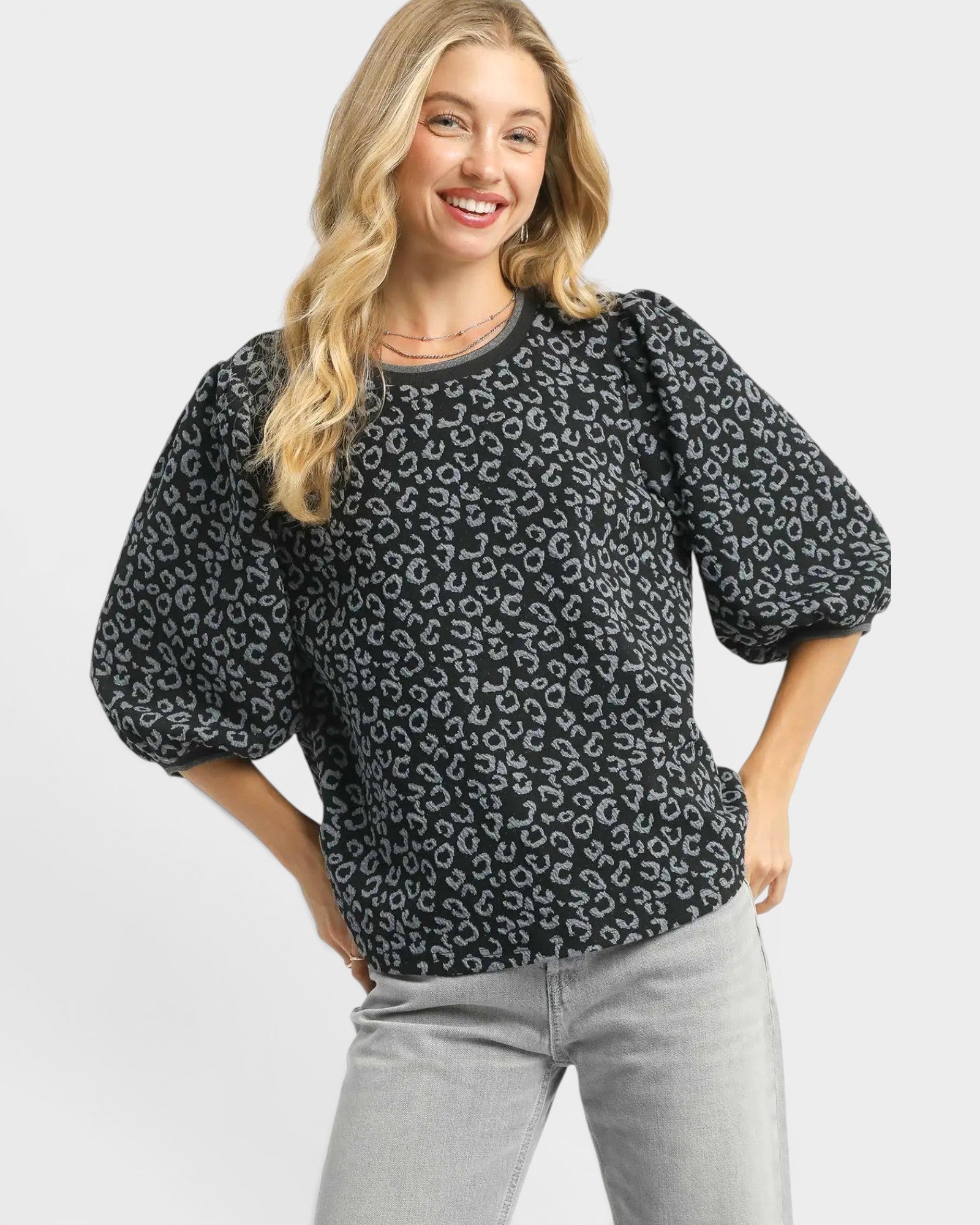 Woman wearing a black leopard print blouse with gray pants on a light gray background
