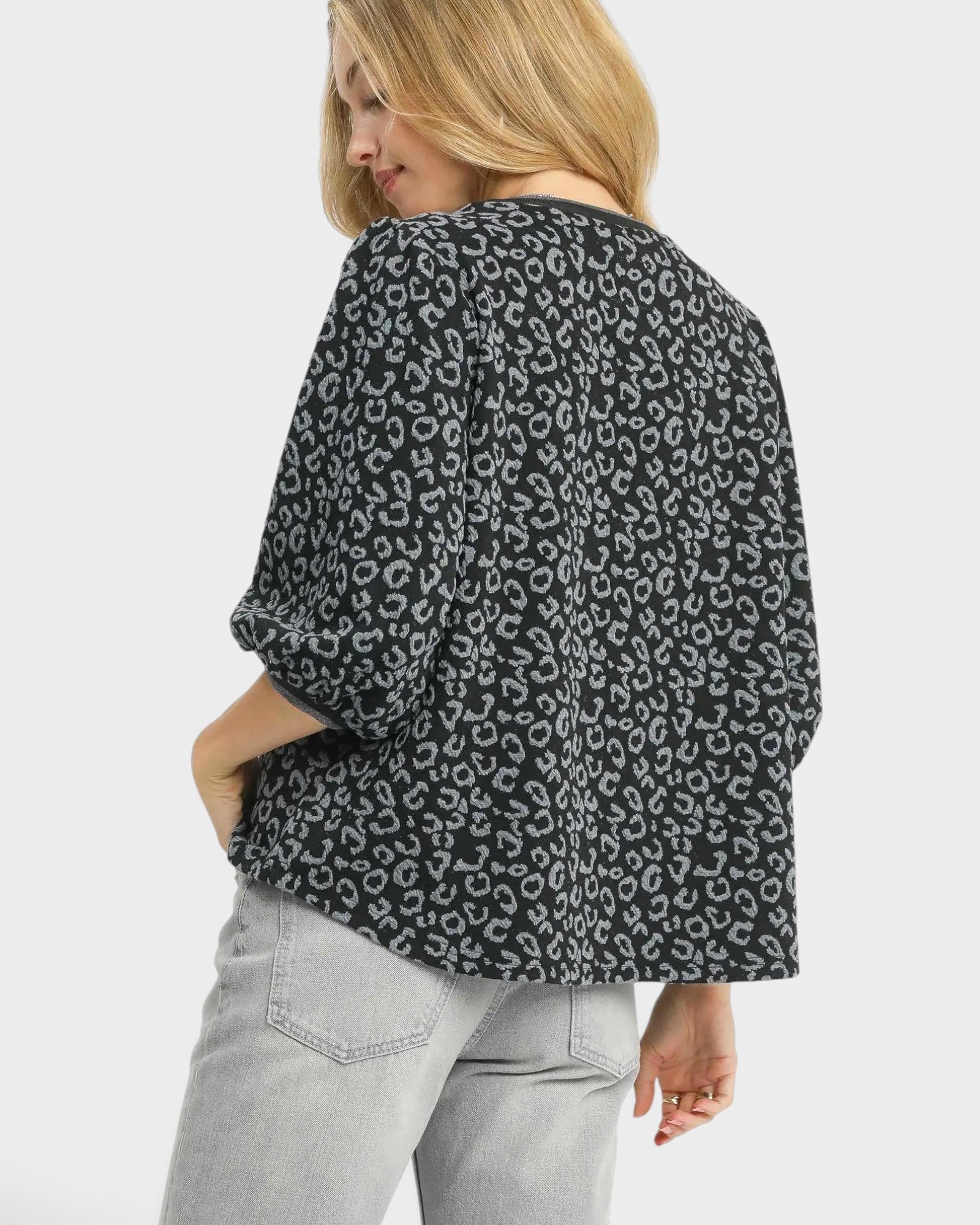 Woman wearing a black and white patterned blouse with light gray pants on a white background