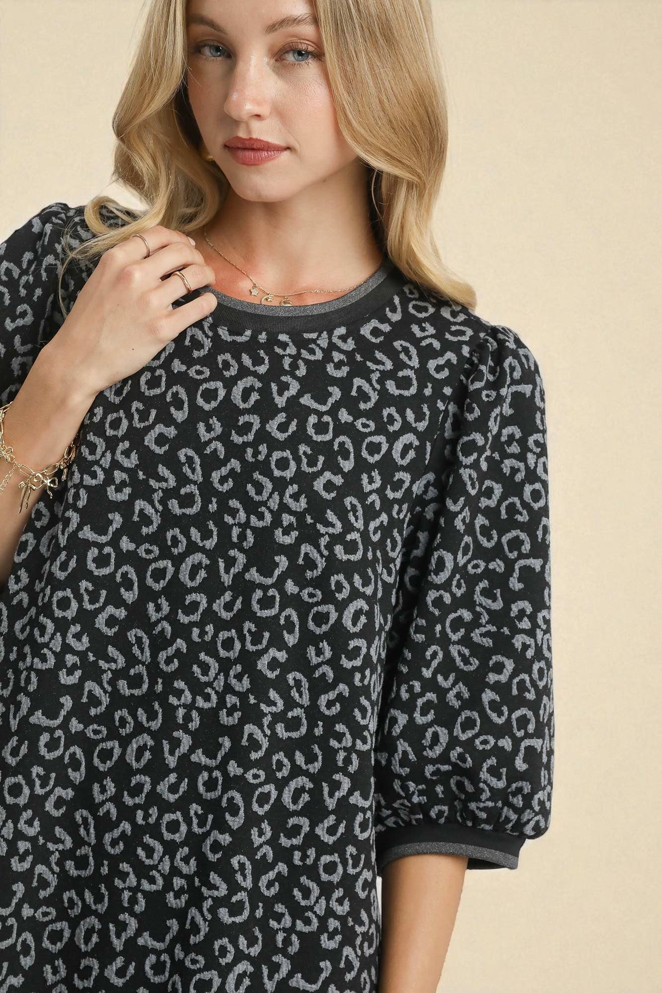 Woman wearing a black and gray leopard print sweater against a beige background