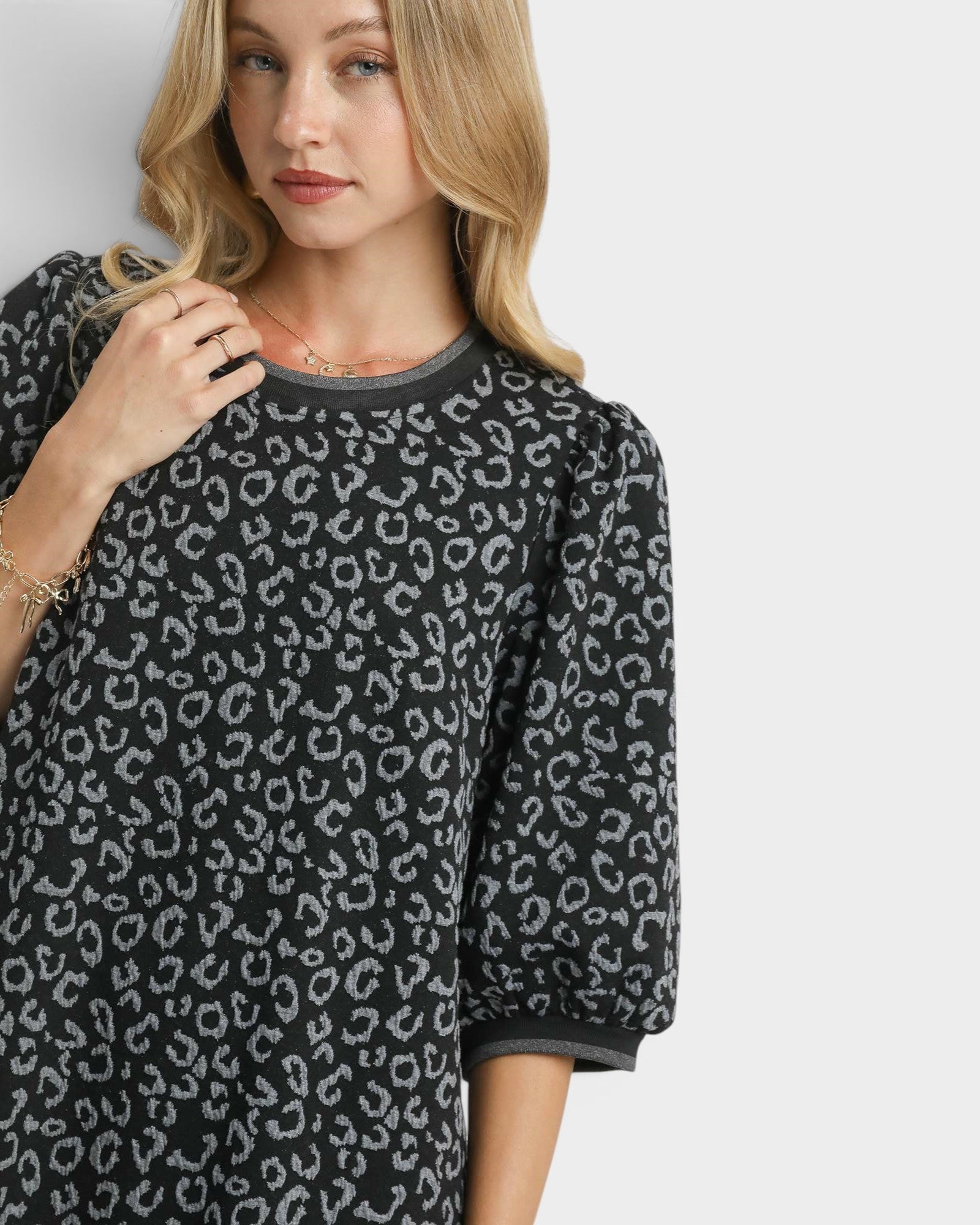 Woman wearing a black dress with a white leopard print pattern on a plain background