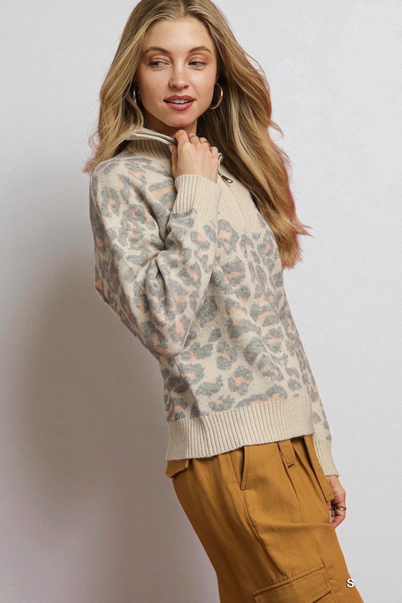 Woman wearing a patterned sweater and brown pants against a plain background