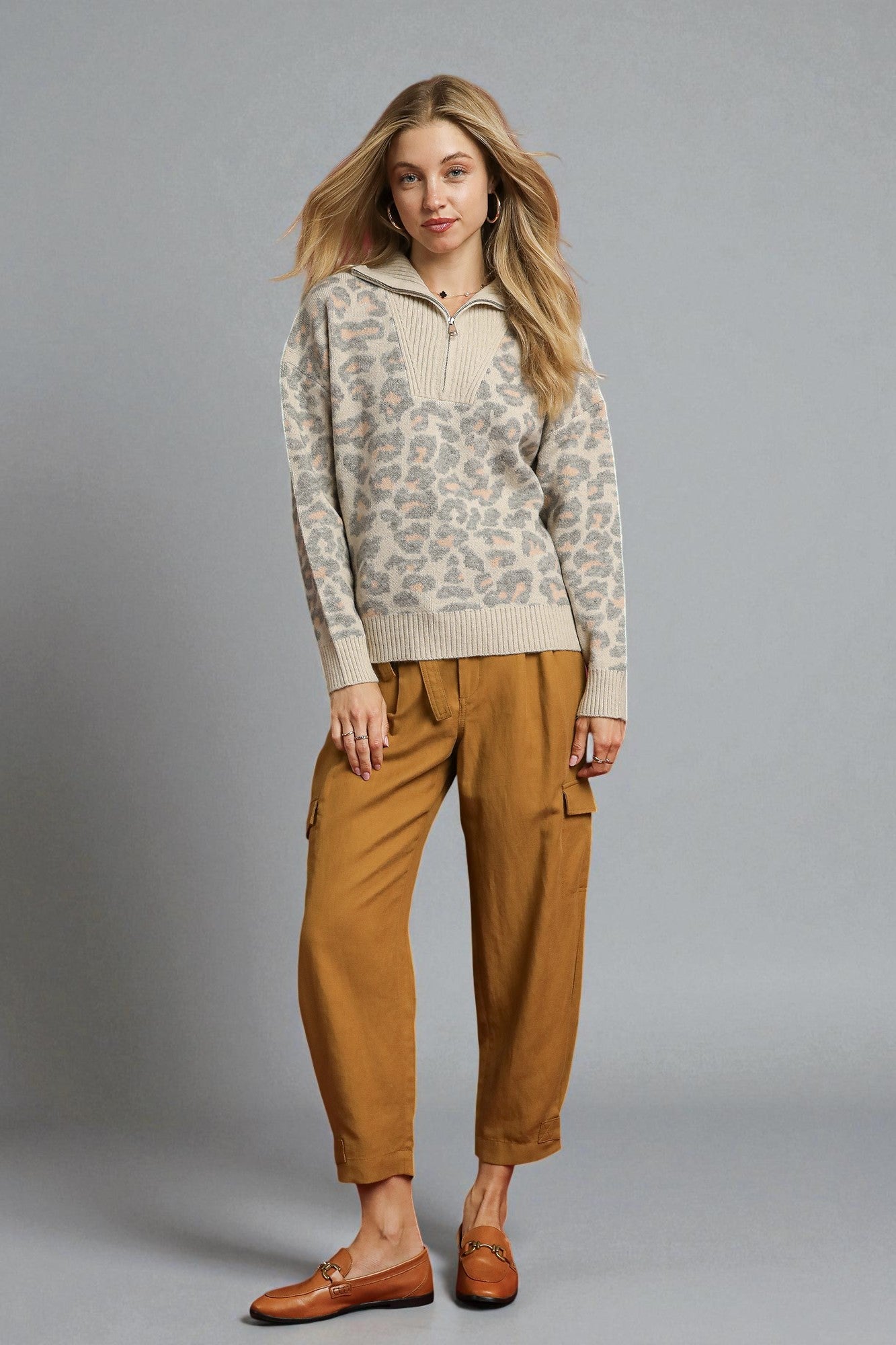 Woman wearing a patterned sweater and tan pants against a gray background