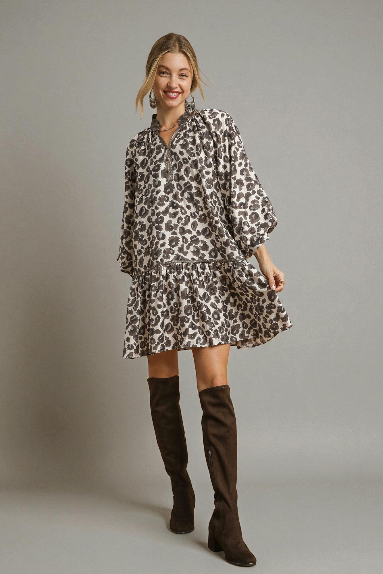 Woman wearing a leopard print dress and brown knee-high boots against a plain background
