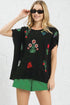 Woman wearing a black top with colorful floral embroidery and green shorts against a white brick wall.