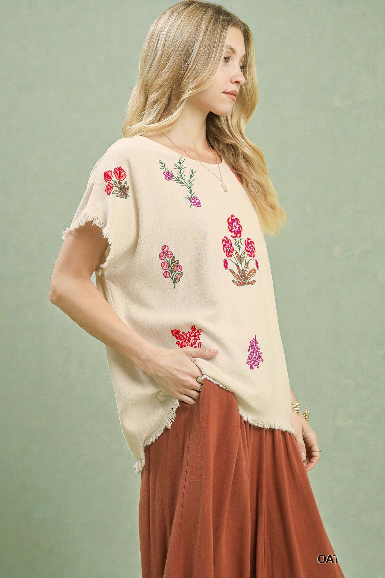 Woman wearing a beige top with floral embroidery on a light green background