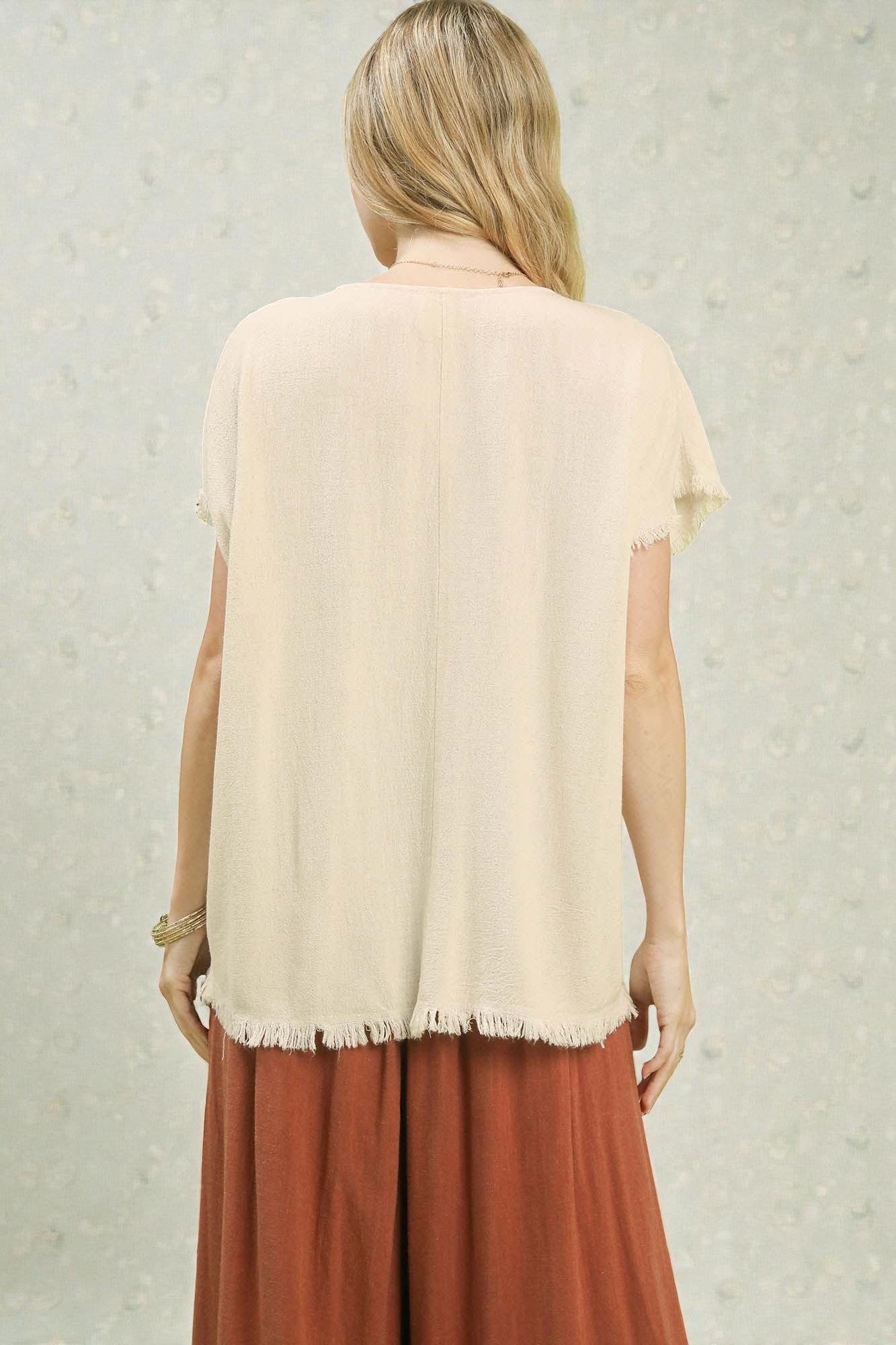 Woman wearing a beige top and brown pants against a light background