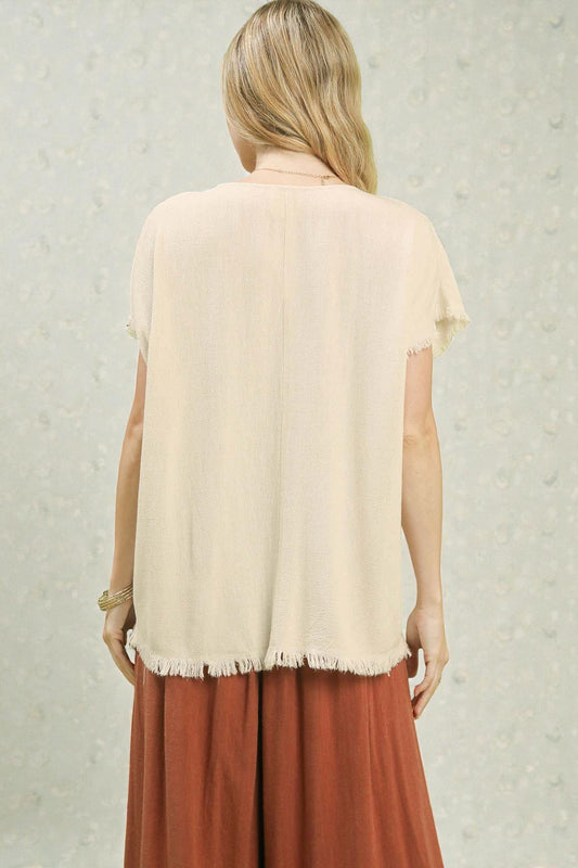 Woman wearing a beige top and brown pants against a light background