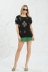 Woman wearing a black embroidered top and green shorts against a white textured background