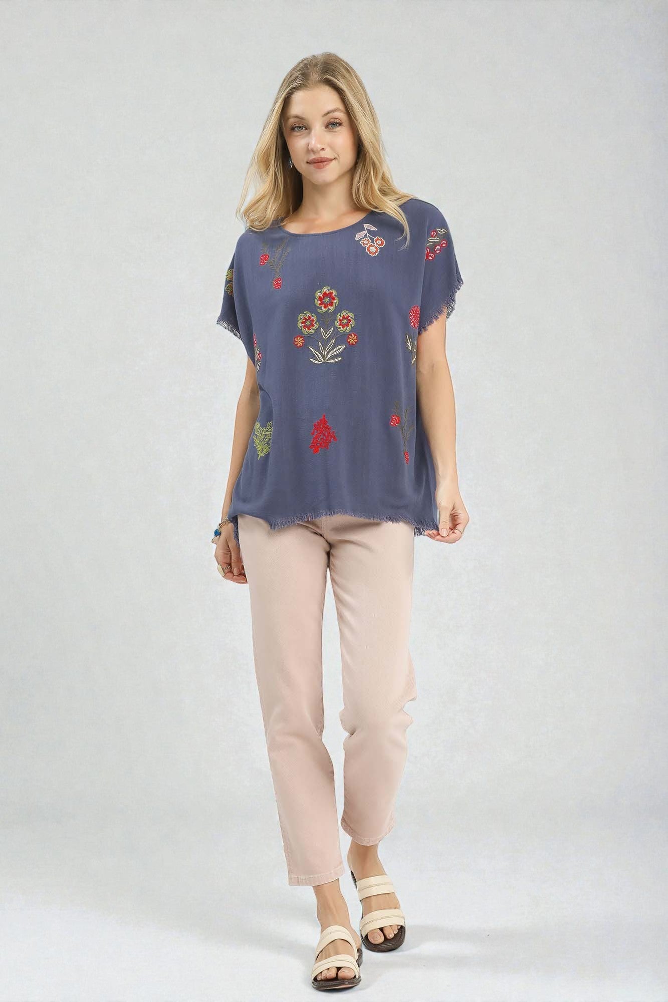 Woman wearing a blue top with floral embroidery and beige pants on a white background