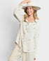 Woman wearing a cream-colored outfit with a wide-brimmed hat against a plain background