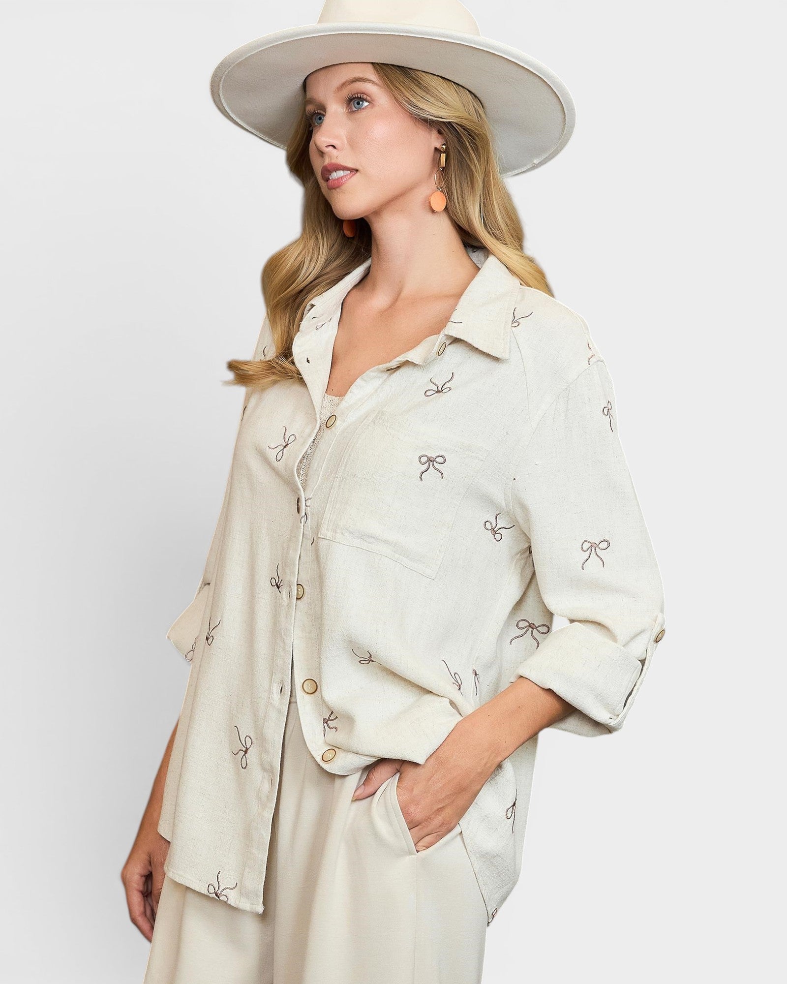 Woman wearing a light-colored outfit with embroidered details and a wide-brimmed hat on a white background