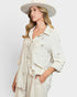Woman wearing a light-colored outfit with embroidered details and a wide-brimmed hat on a white background