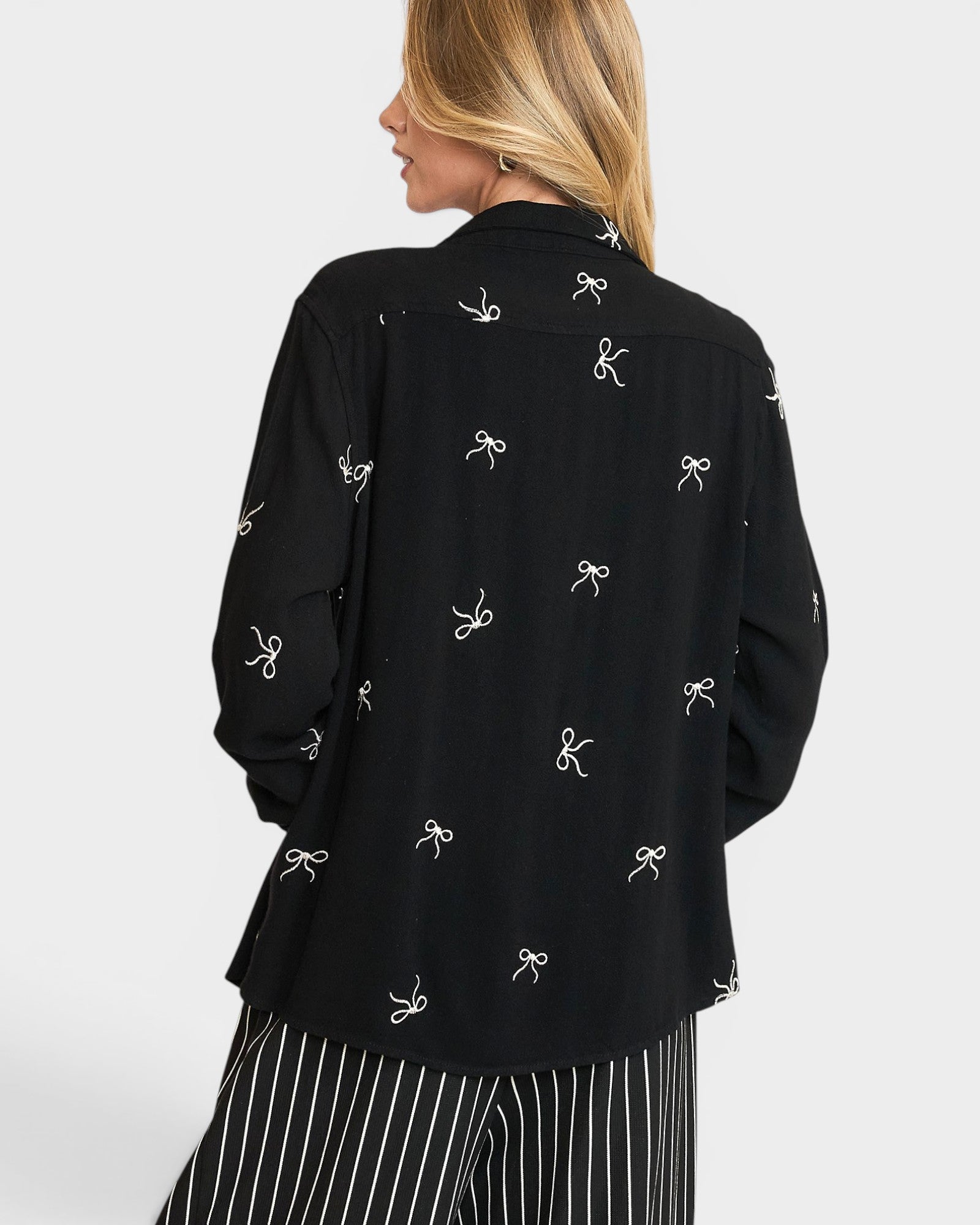 Black blouse with white bow pattern worn by a person on a light gray background