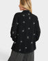 Black blouse with white bow pattern worn by a person on a light gray background