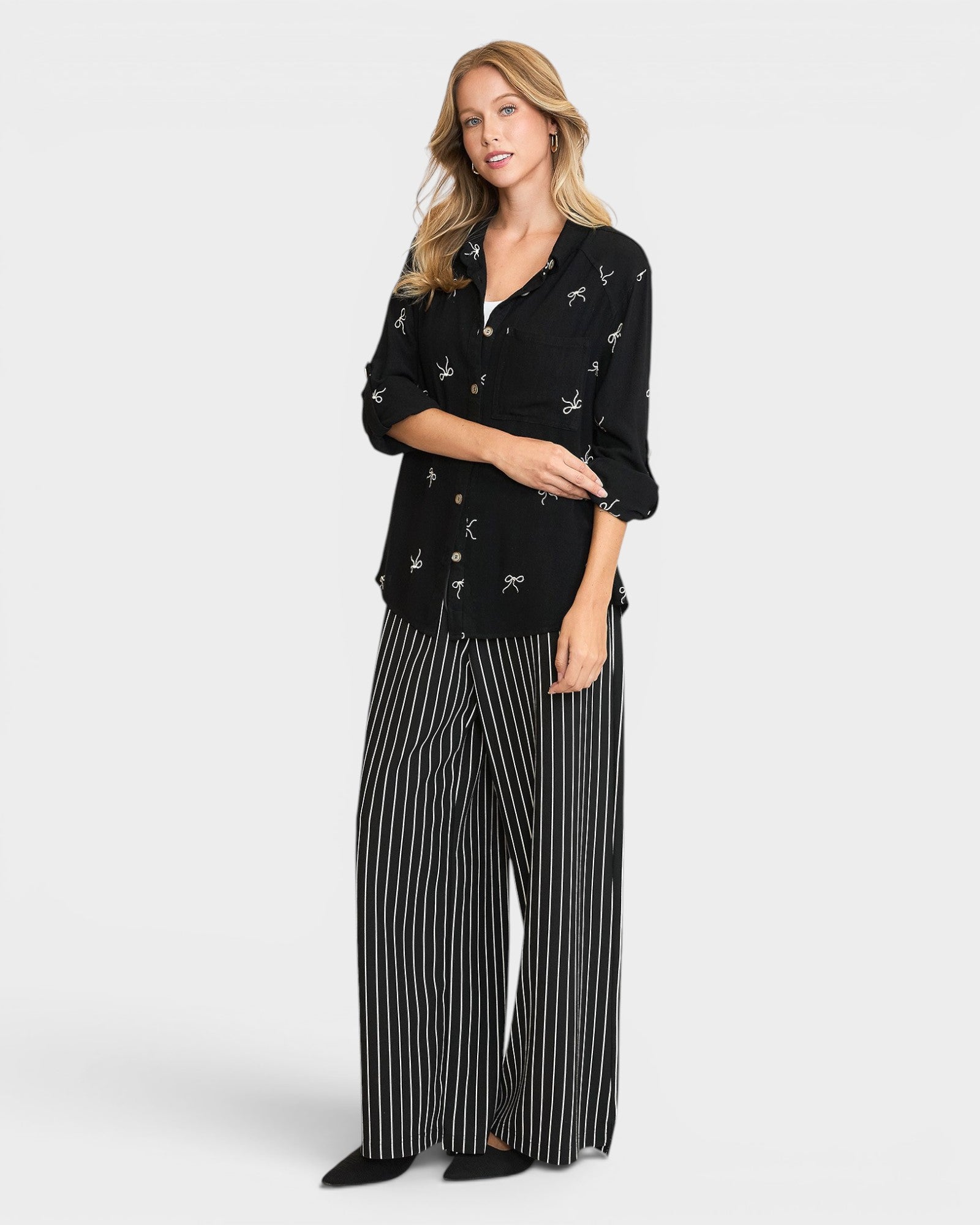 Woman wearing a black patterned top and striped pants on a white background