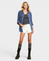 Woman wearing a blue denim shirt, black tank top, white shorts, and black boots on a white background