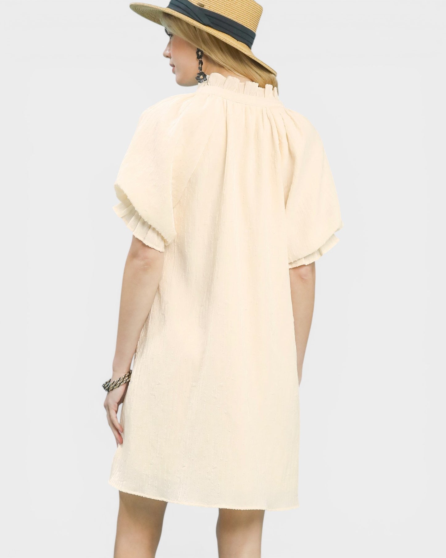 Woman wearing a light-colored dress and straw hat on a plain background