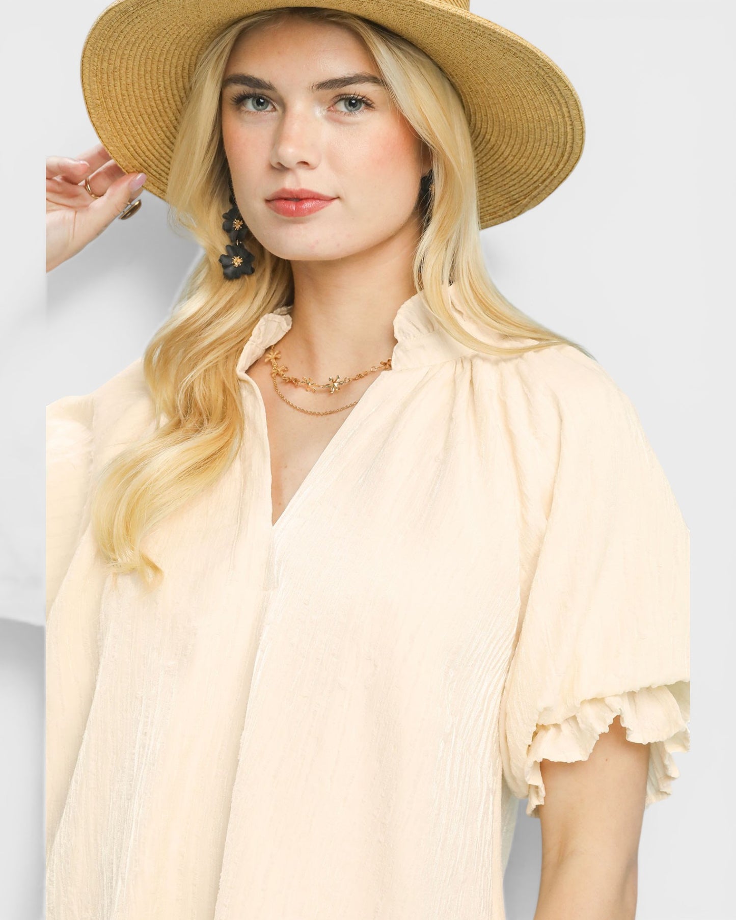 Woman wearing a beige hat and blouse with ruffled sleeves on a light gray background