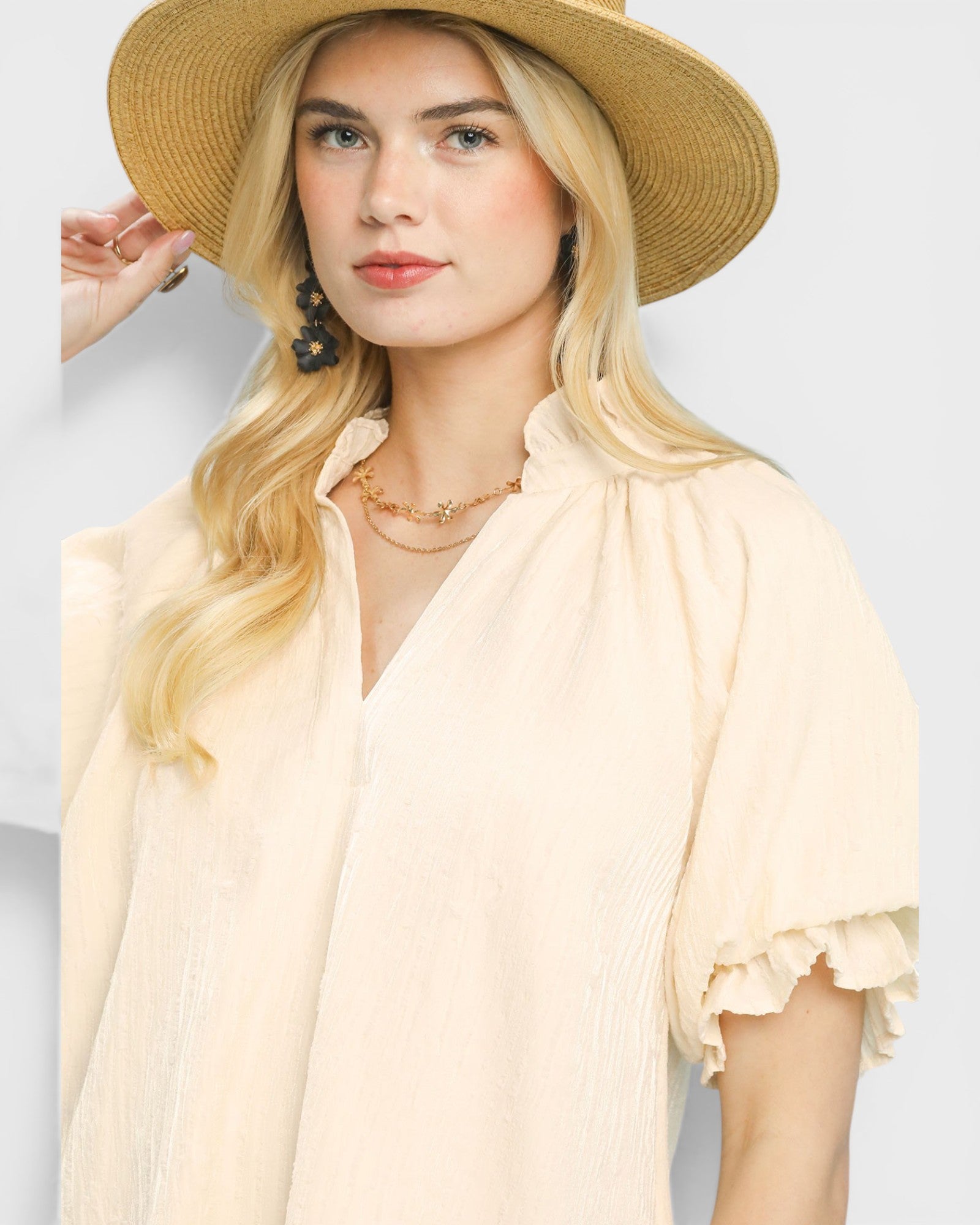 Woman wearing a beige hat and blouse with ruffled sleeves on a light gray background