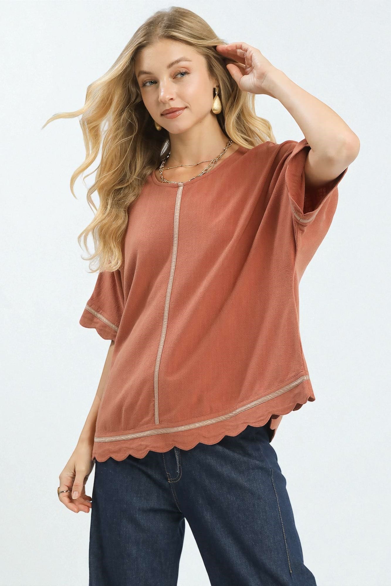 Woman wearing a rust-colored blouse with scalloped edges on a white background
