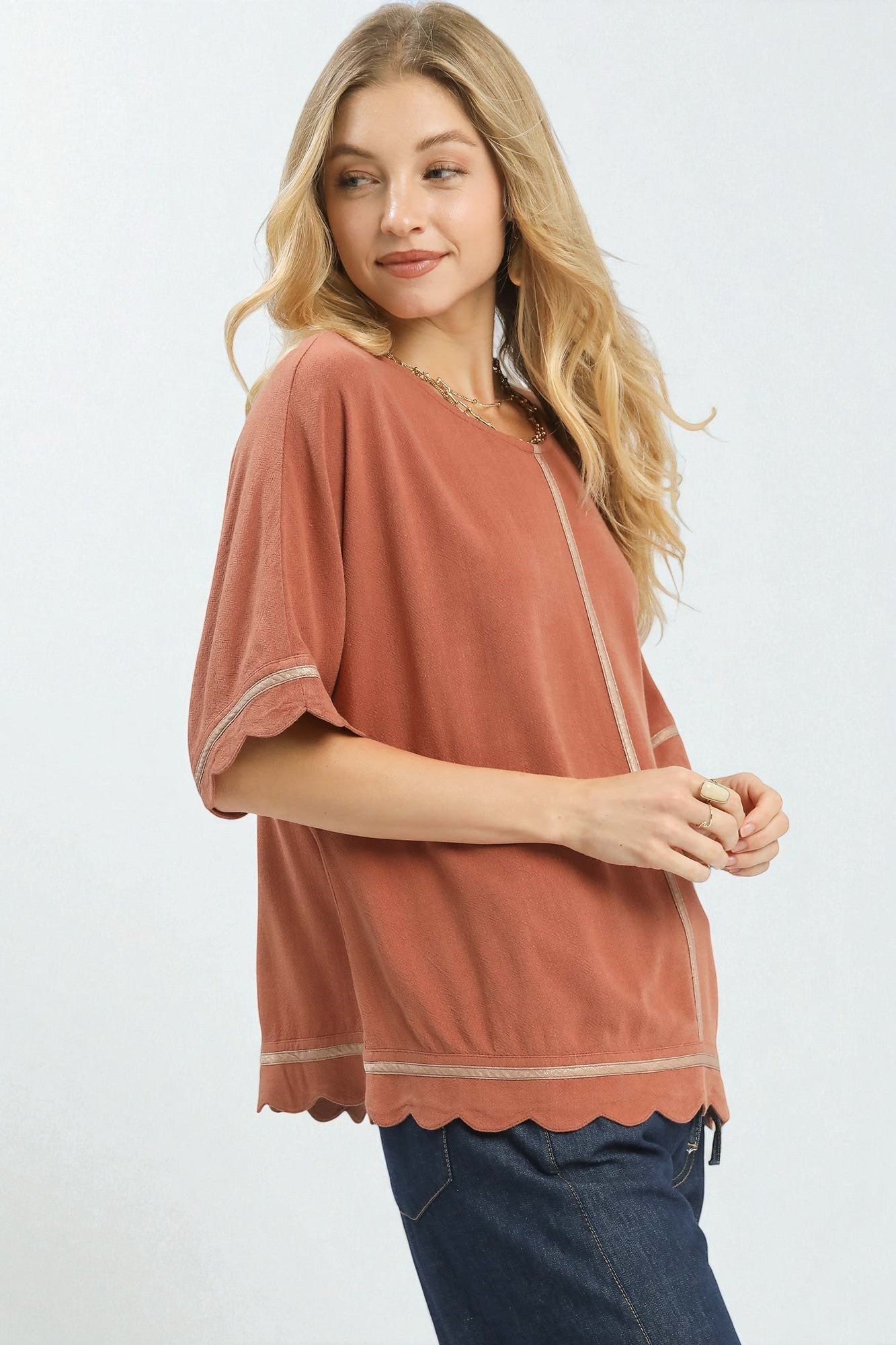 Woman wearing a rust-colored top with scalloped edges on a white background