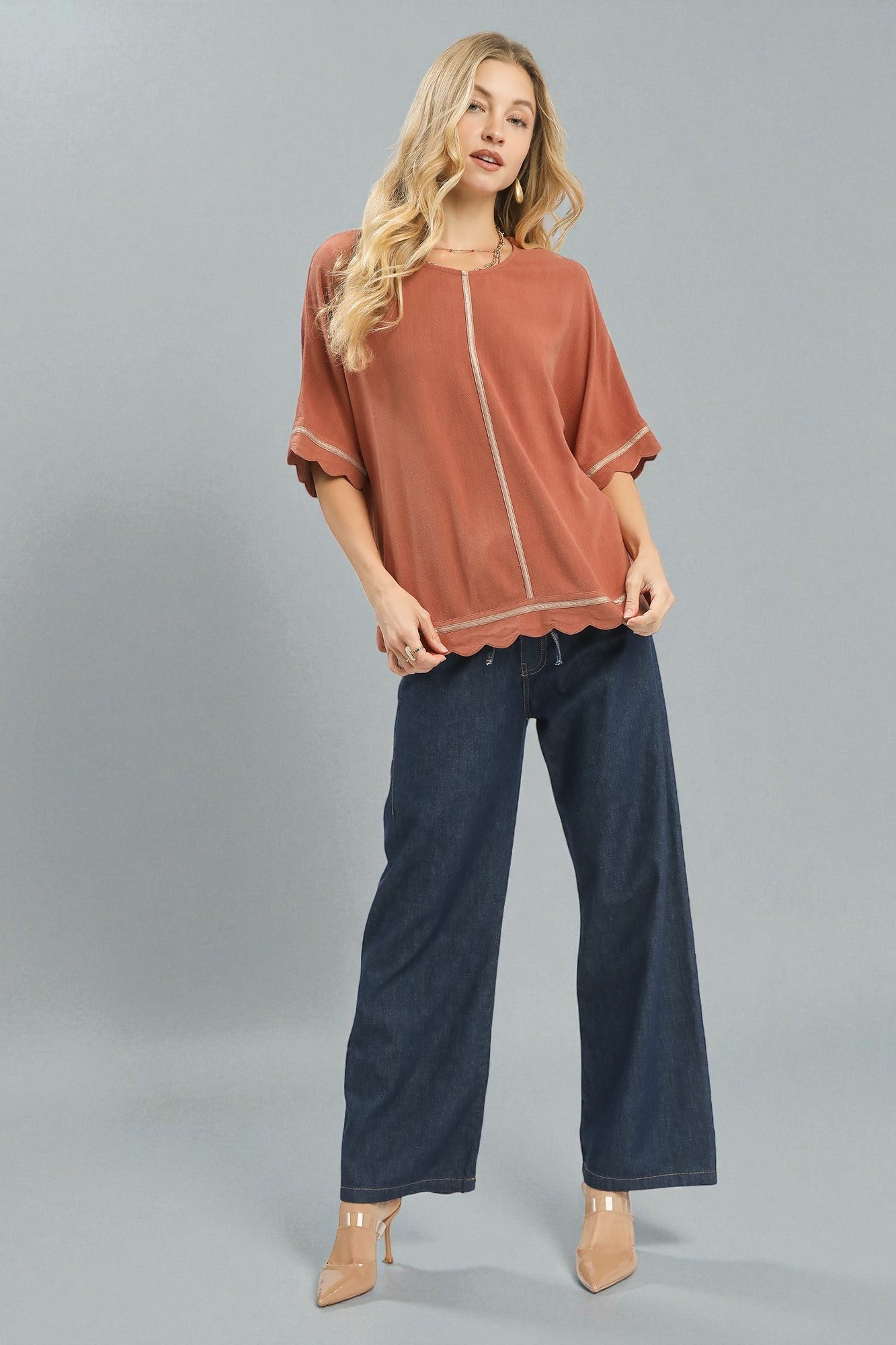 Woman wearing a rust-colored top and dark blue jeans on a gray background