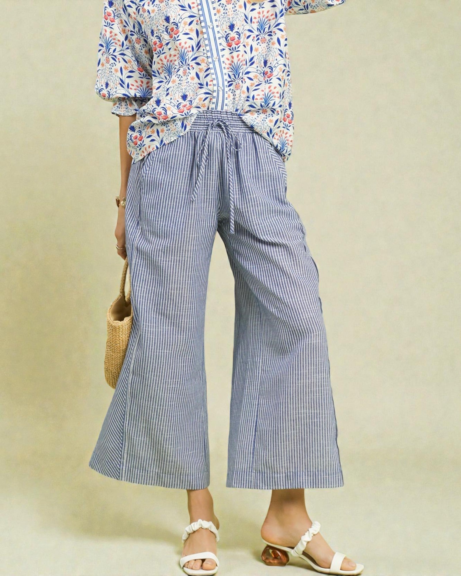 Person wearing a floral blouse and blue striped pants on a beige background