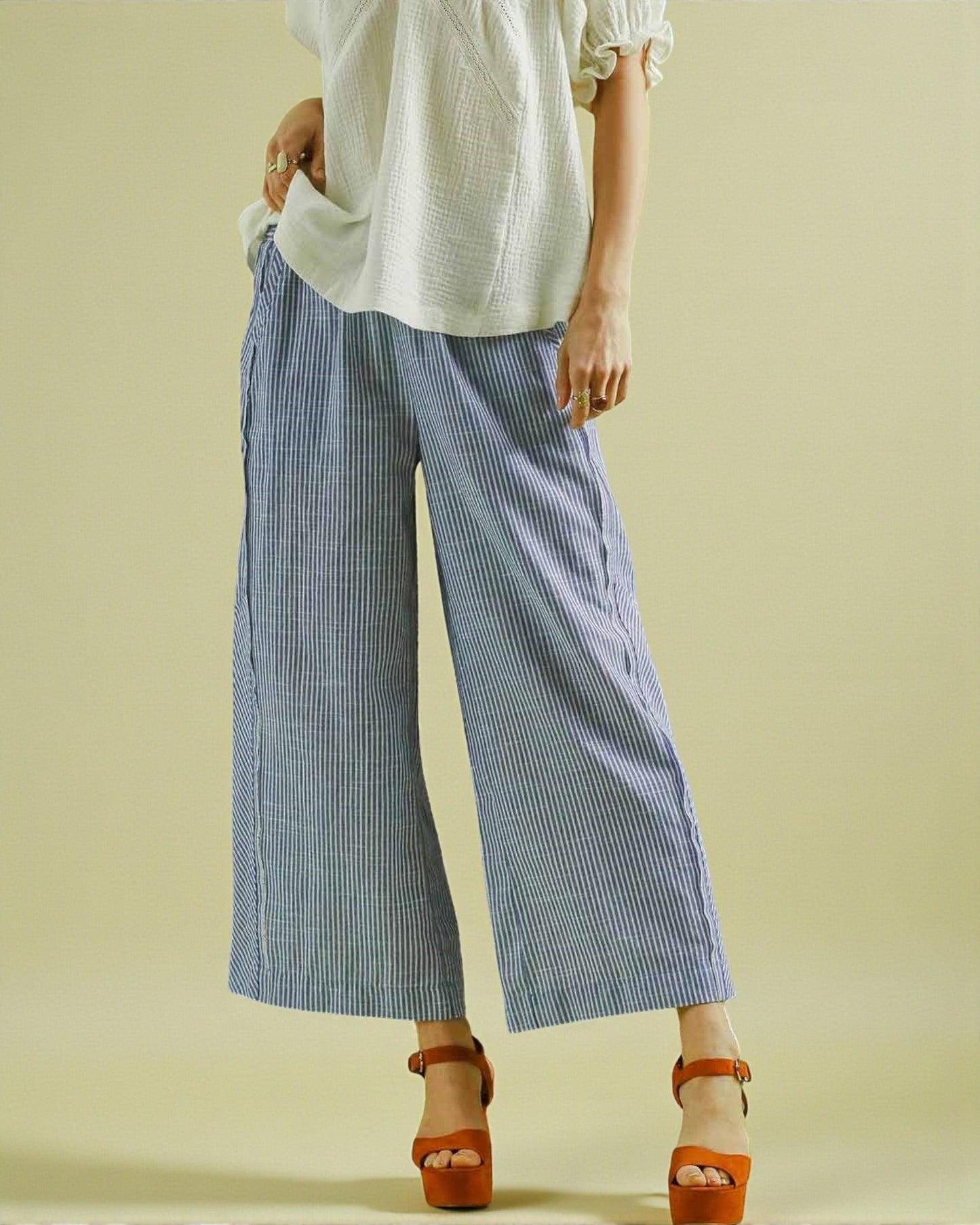 Person wearing a white top and blue striped pants on a beige background