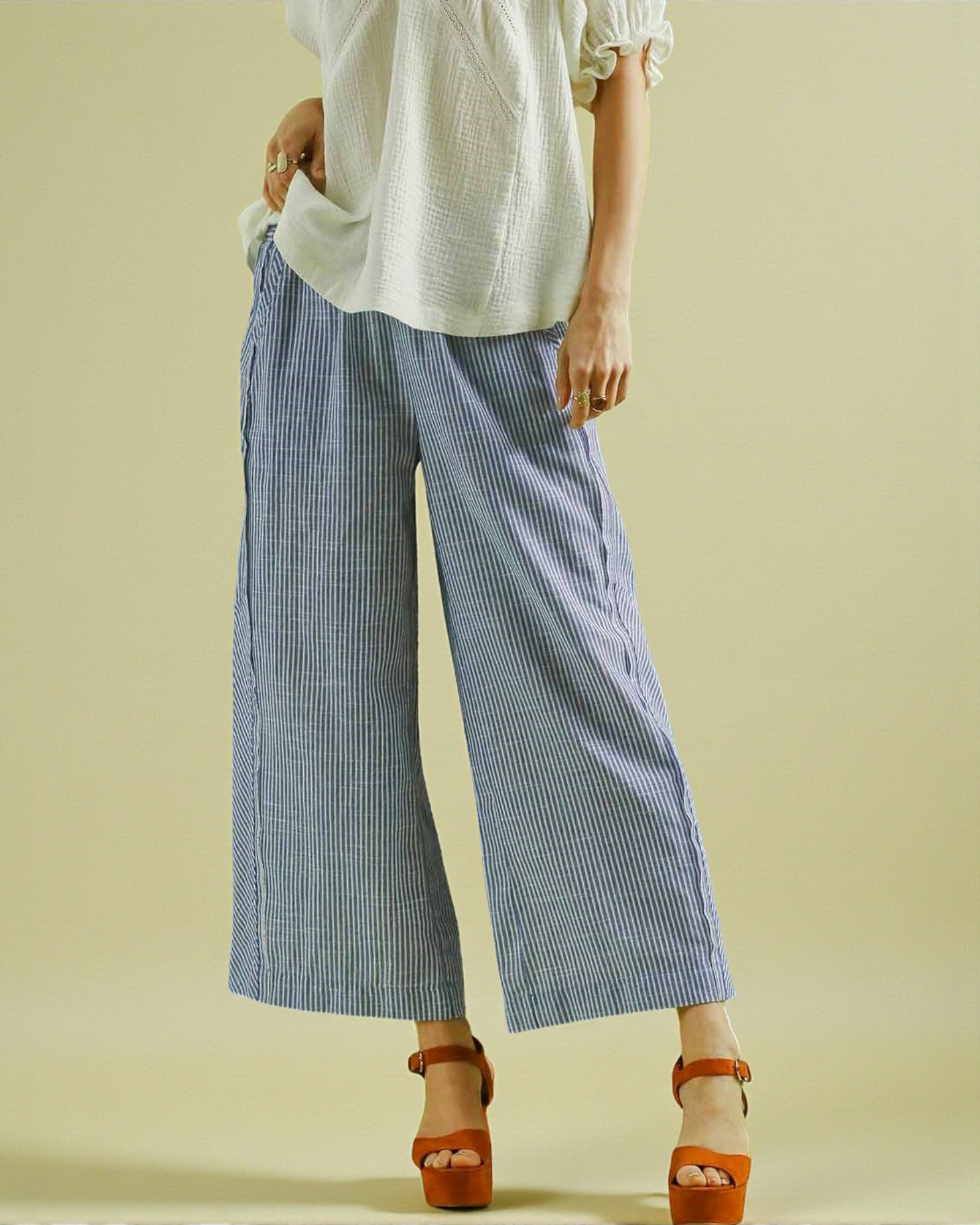 Person wearing a white top and blue striped pants on a beige background