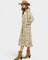 Woman wearing a long floral dress with long sleeves, brown boots, and a wide-brimmed hat on a white background.