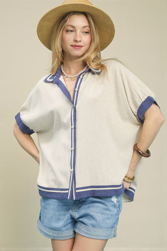 Woman wearing a white shirt with blue trim, denim shorts, and a straw hat on a plain background