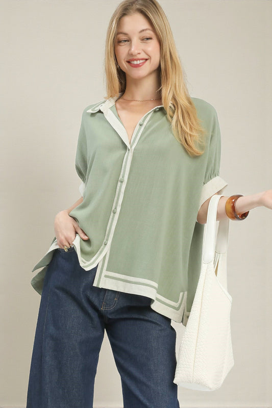 Woman wearing a green shirt with a white collar and blue jeans, holding a white bag.