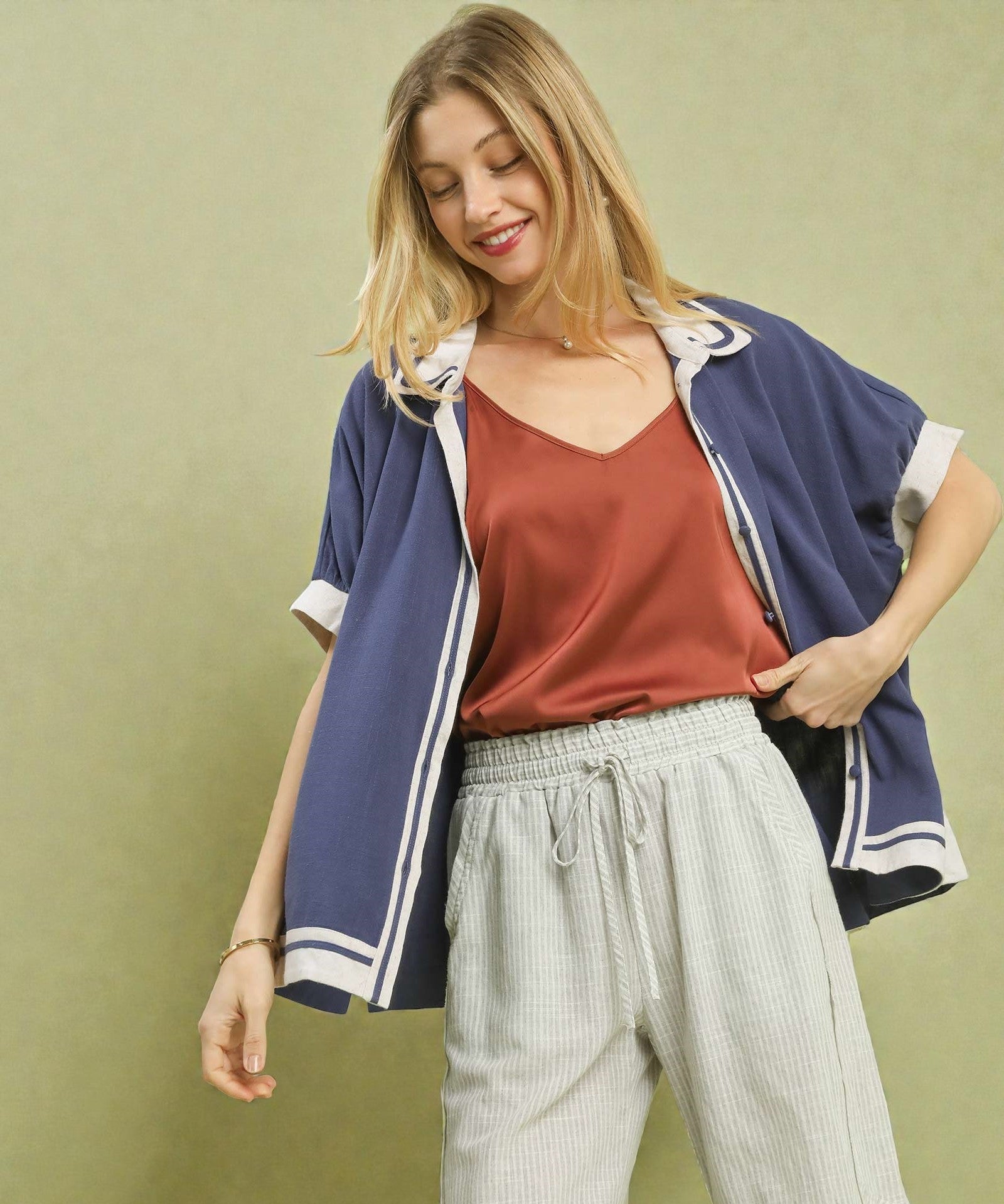 Woman wearing a blue jacket over a red top and light pants on a green background