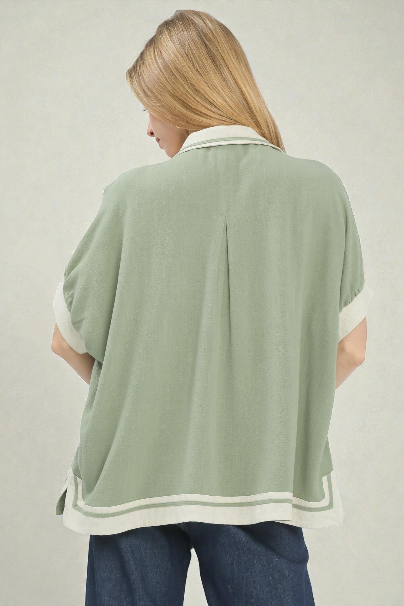 Woman wearing a green poncho with white trim on a plain background