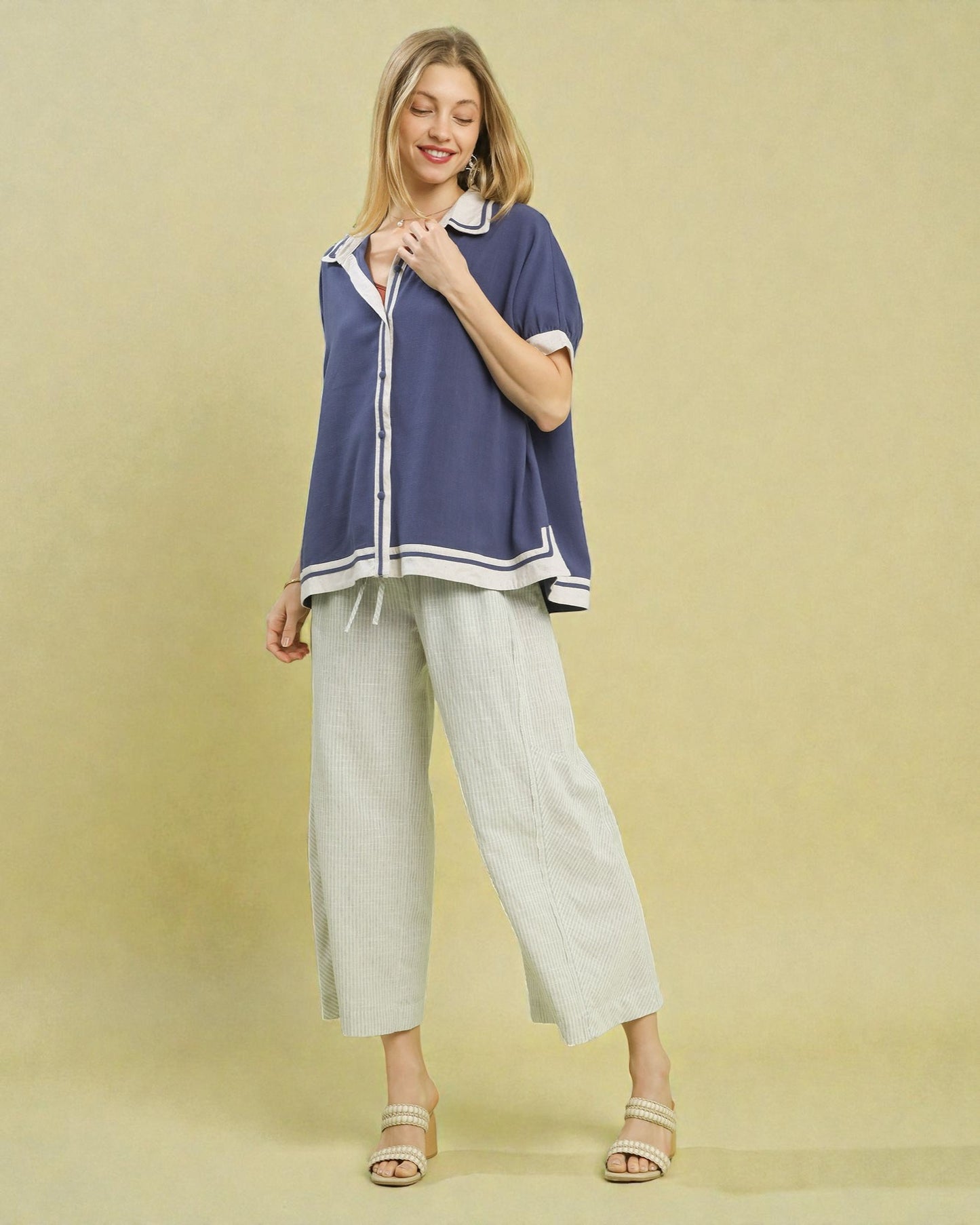 Woman wearing a blue top and light gray pants on a beige background